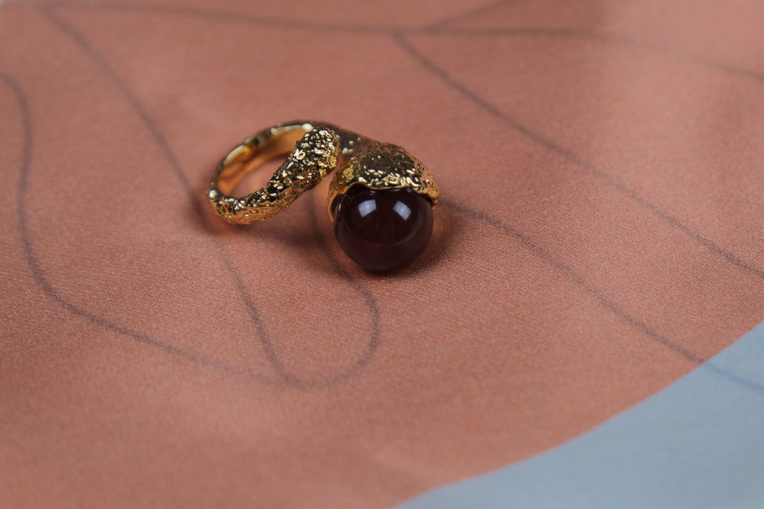 Une bague composée une cristal rouge et cuivre plaqué or 18k posée sur une écharpe en soie 