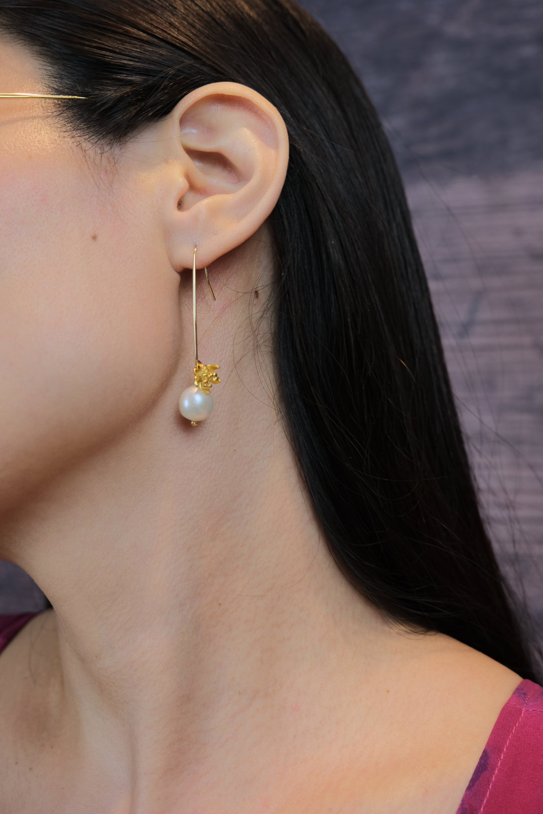 Une jeune femme porte des boucles d’oreilles élégantes avec une perle en or laminé 14k, résistantes à l’eau. La perle brille délicatement, ajoutant une touche de sophistication à son style. Le design moderne des boucles d’oreilles complète parfaitement sa tenue, offrant un look raffiné et élégant, idéal pour toutes les occasions.