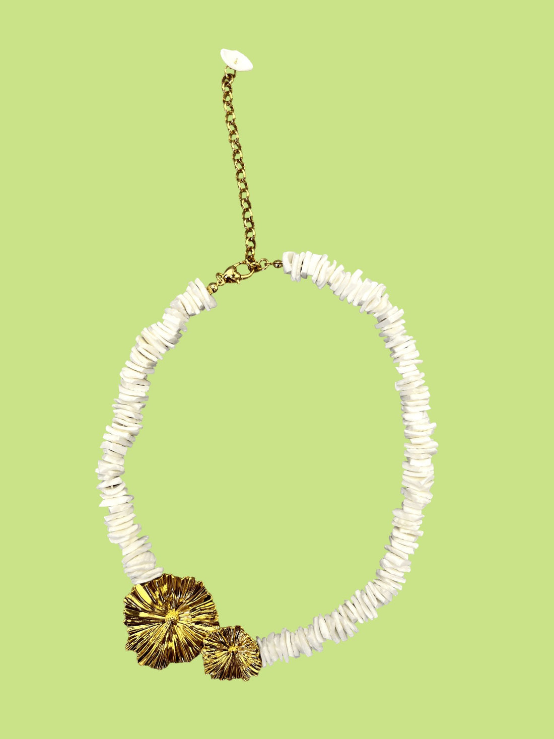 Un collier orné de coquillages naturels et de deux fleurs en laiton plaqué or 18 carats, délicatement posé sur une écharpe en soie. Les détails dorés des fleurs contrastent élégamment avec la texture douce de la soie et les coquillages, créant une harmonie parfaite entre nature et raffinement