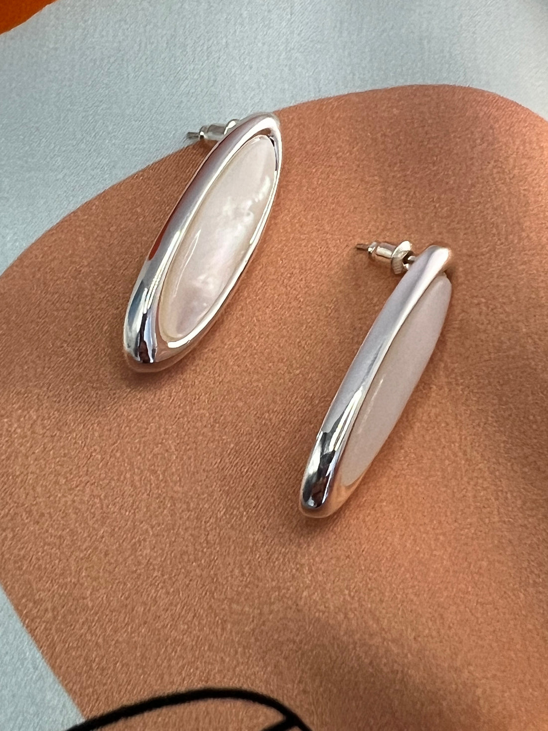  élégant  boucles d’oreilles en nacre et cuivre plaqué argent, reposant sur une écharpe en soie. La douceur de la nacre et la brillance de l’argent créent une composition harmonieuse, idéale pour sublimer toute tenue avec une élégance subtile.